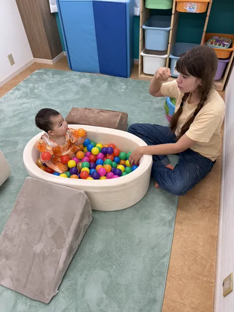 プリスクールで先生に見守られながらボールプールで遊ぶ赤ちゃん