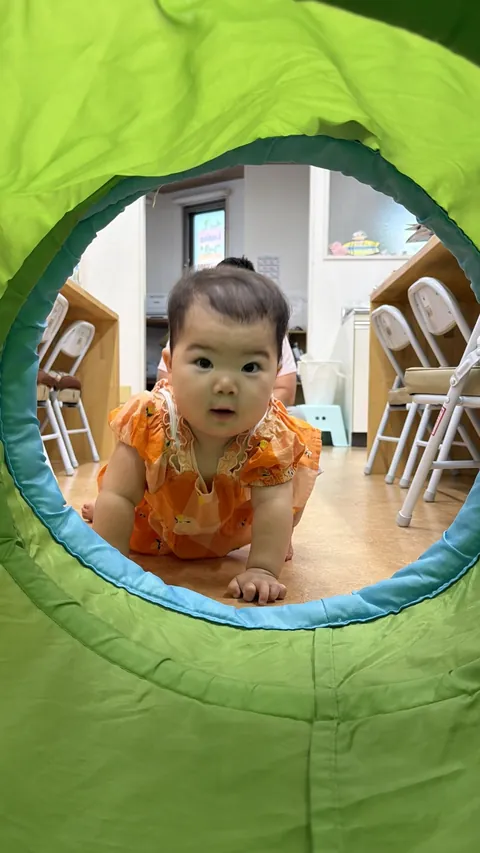 プリスクールでトンネルの向こうからはいはいでこちらを見る赤ちゃん