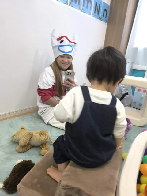 プリスクールのハロウィンの日、クッションの坂にまたがって遊ぶ赤ちゃんと見守る先生