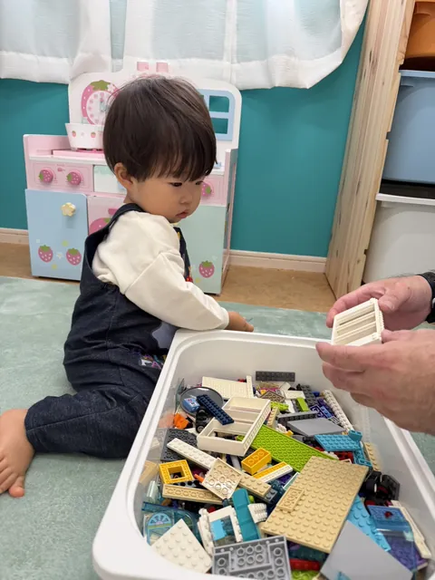 先生と一緒に、ブロックの箱からパーツを取り出して遊ぶプリスクールの子ども