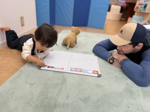 先生と一緒に、ホワイトボードに顔のマグネットを並べる子ども