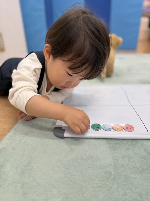 ホワイトボードに表情のちがう顔のマグネットを一つずつ並べる子ども