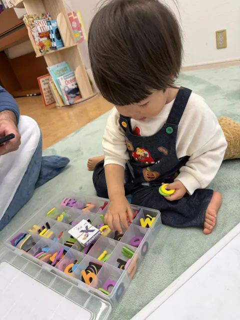 アルファベットのフォームレターの箱から文字を選ぶ子ども