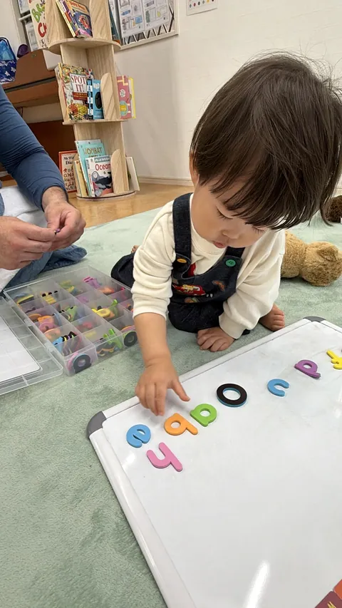 ホワイトボードに並べたアルファベットを指さす子ども