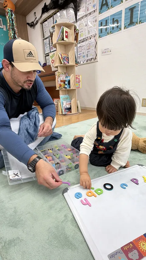 先生から文字を受け取りながら、ホワイトボードにアルファベットを並べる子ども