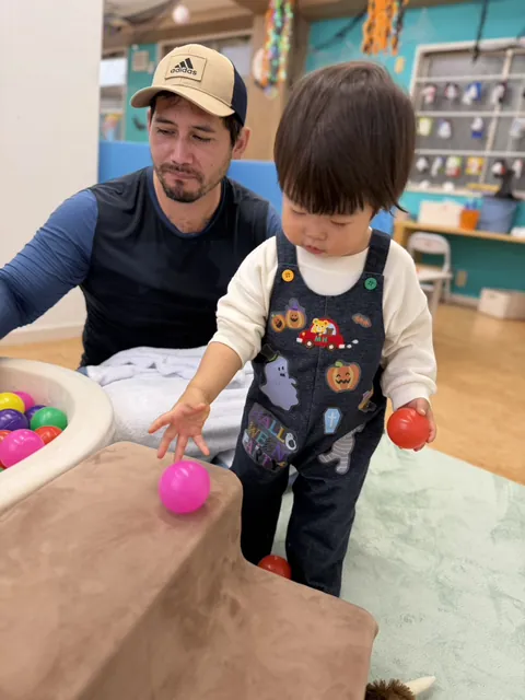 先生が見守る中、段差の上からボールを転がす子ども