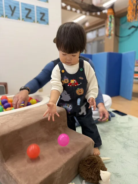 ハロウィン柄のオーバーオールで、段差からボールを転がして遊ぶ子ども