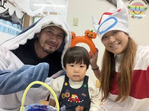 サメの着ぐるみの先生とハロウィンの帽子の先生と一緒に記念撮影する子ども