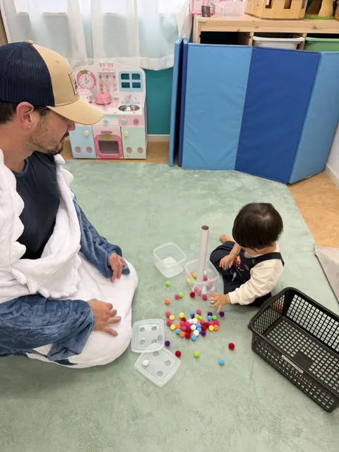 先生と一緒に、紙の筒にポンポンを入れて遊ぶ子ども