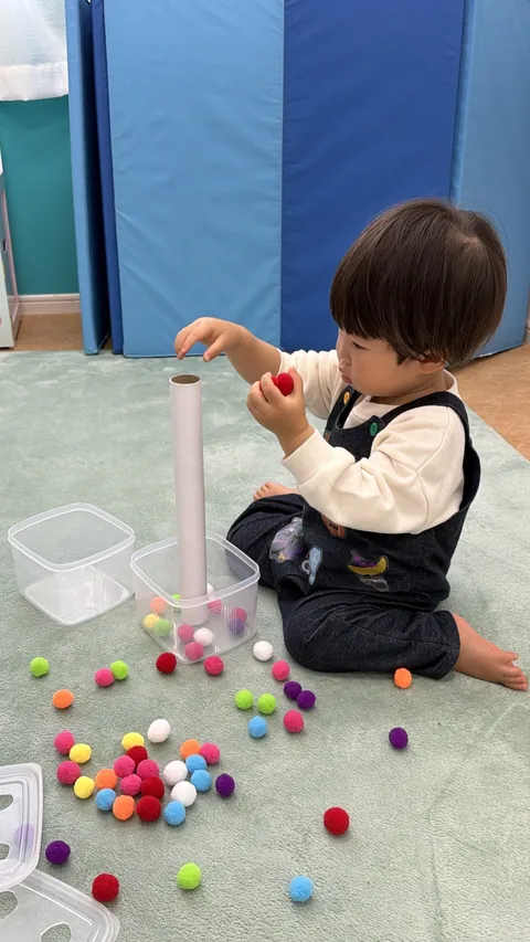 紙の筒にカラフルなポンポンを落として遊ぶ子ども