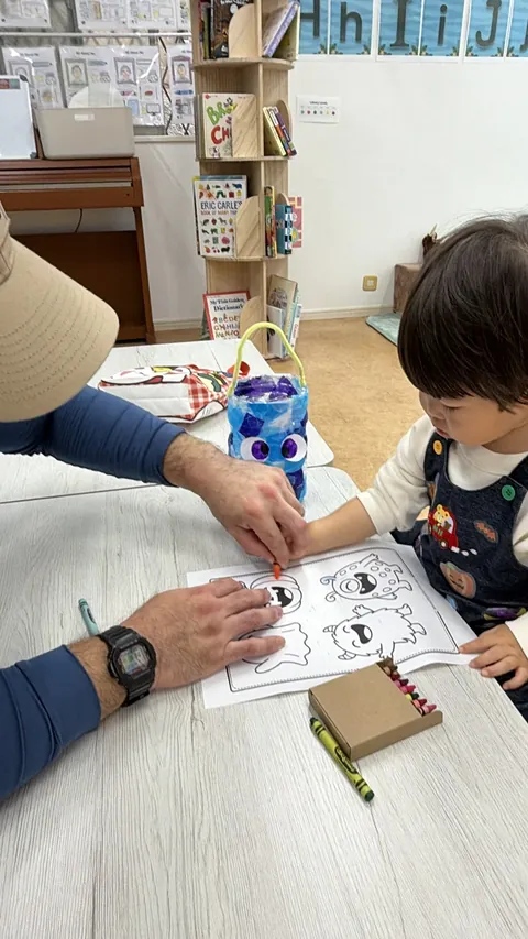 先生と一緒に、モンスターのぬり絵をクレヨンで塗る子ども