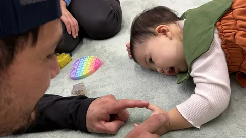 床に寝そべって、先生の指にタッチして笑う赤ちゃん