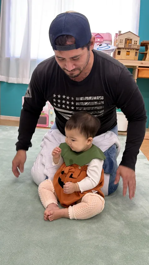 かぼちゃの衣装を着て、先生の前にすわる赤ちゃん