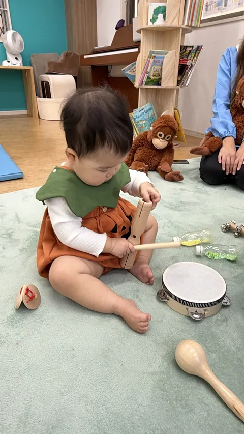 かぼちゃの衣装で、木の楽器をばちでたたいて遊ぶ赤ちゃん