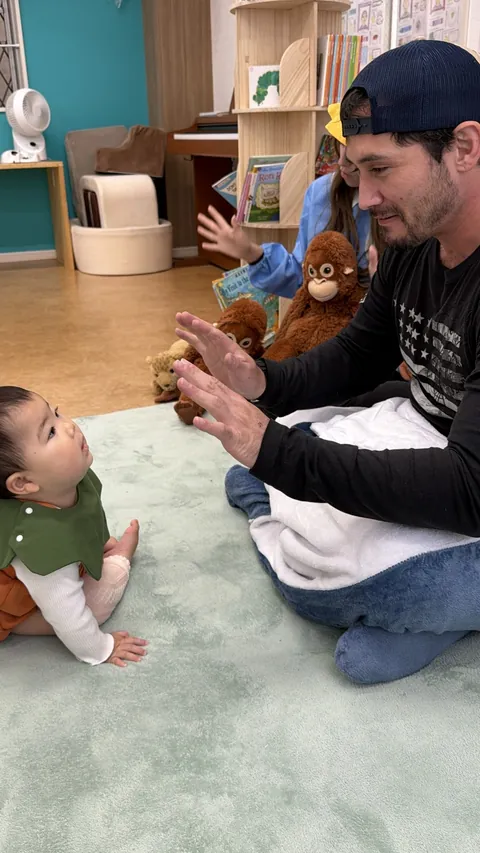 先生の手遊びをじっと見上げる、かぼちゃの衣装の赤ちゃん