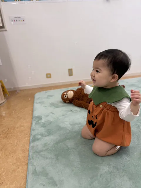 シャボン玉に手を伸ばして笑顔を見せる、かぼちゃの衣装の赤ちゃん