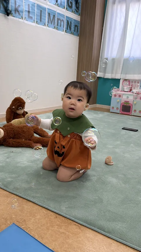 ふわふわ浮かぶシャボン玉に囲まれる、かぼちゃの衣装の赤ちゃん