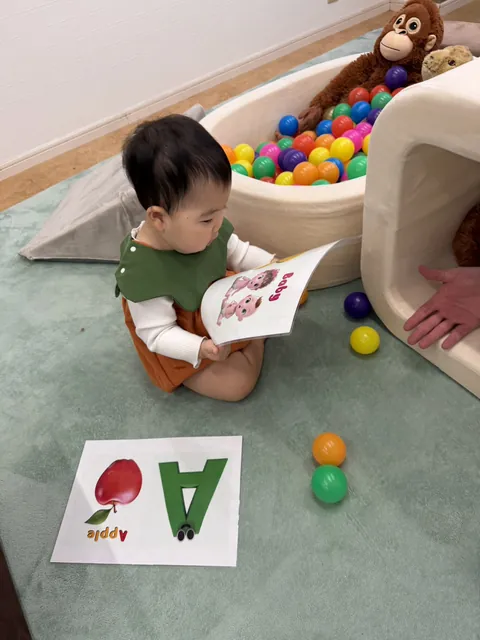 ボールプールのそばで、「Baby」のアルファベットカードを見る赤ちゃん