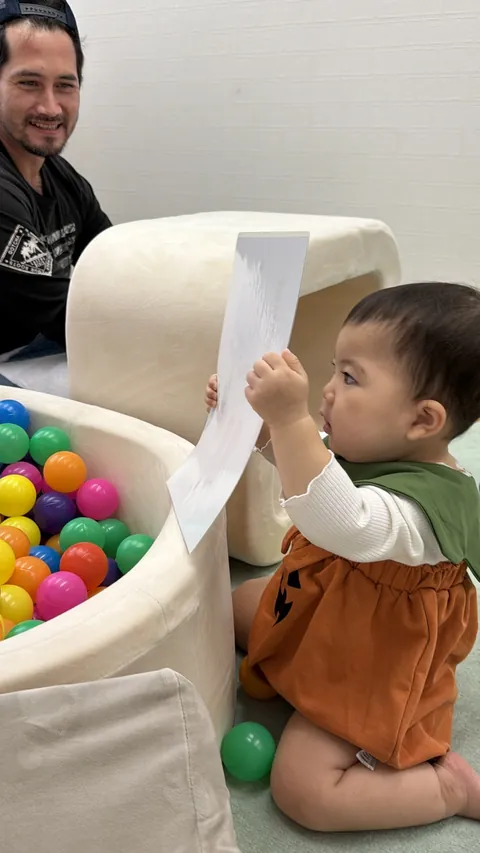 先生が見守る中、カードを高く持ち上げる赤ちゃん