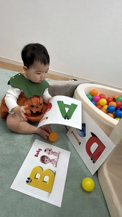 「A」のアルファベットカードを手に持って見る赤ちゃん