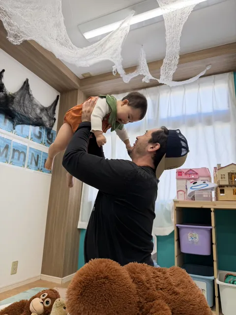 先生に高く抱き上げてもらう、かぼちゃの衣装の赤ちゃん