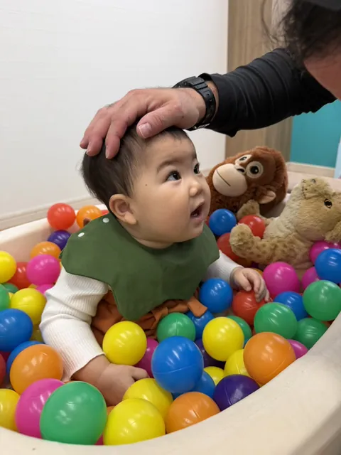 ボールプールの中で、先生に頭をなでてもらう赤ちゃん