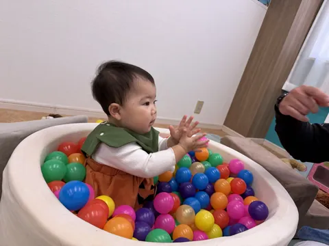 ボールプールの中で、両手でボールを持つ赤ちゃん