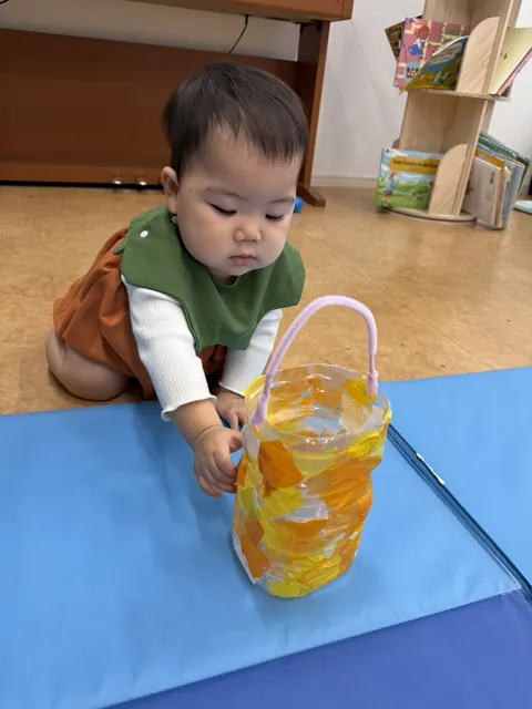 オレンジと黄色のセロファンで作ったハロウィンバケツに手を伸ばす赤ちゃん