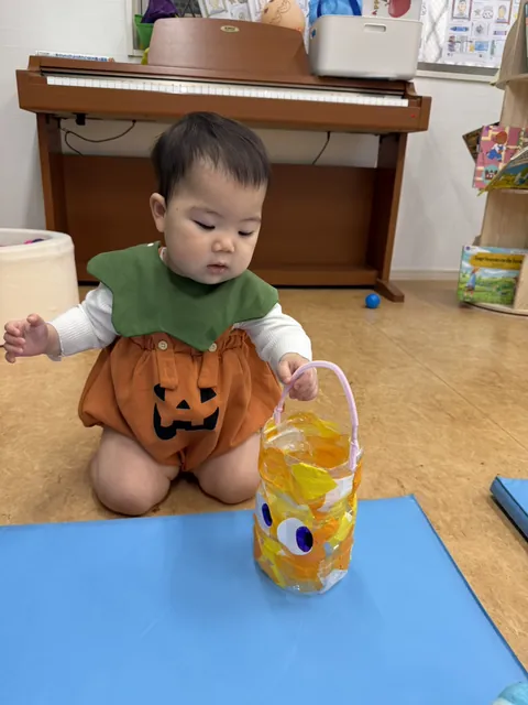 手作りのハロウィンバケツの持ち手をつかむ、かぼちゃの衣装の赤ちゃん