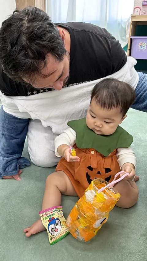 サメの着ぐるみの先生と一緒に、お菓子と手作りバケツで遊ぶ赤ちゃん