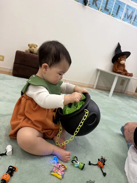 魔女の大鍋に手を入れて、中のおもちゃを探す赤ちゃん