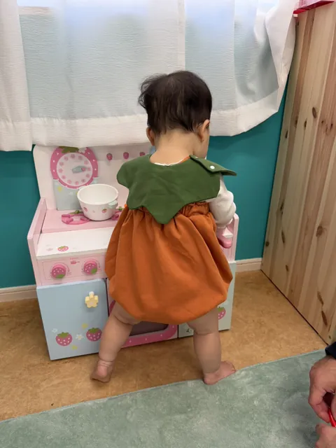 おもちゃのキッチンの前に立って遊ぶ、かぼちゃの衣装の赤ちゃん