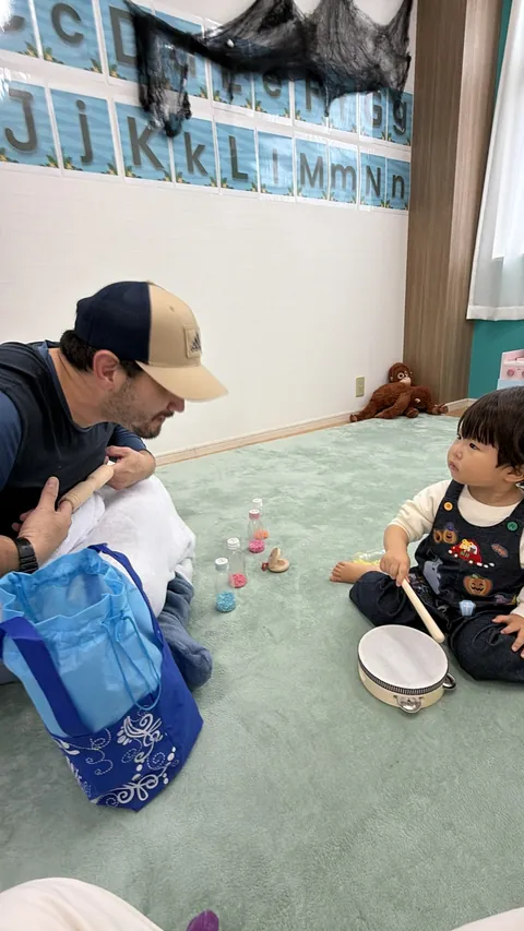 先生と向かい合って、タンバリンやシェイカーで音楽遊びをする子ども