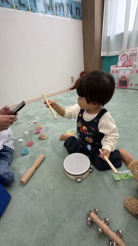 ばちを持ってタンバリンをたたこうとする、ハロウィン柄のオーバーオールの子ども