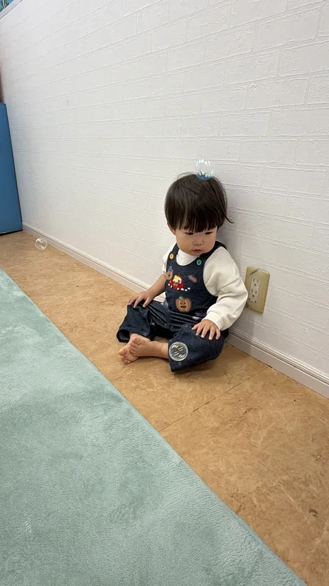 壁にもたれて、頭にのったシャボン玉を見つめる子ども