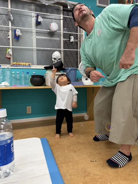 プリスクールで先生と一緒にシャボン玉を指さして見上げる赤ちゃん