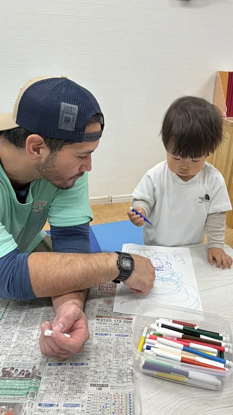 プリスクールで先生のとなりでペンを使ってお絵かきする赤ちゃん