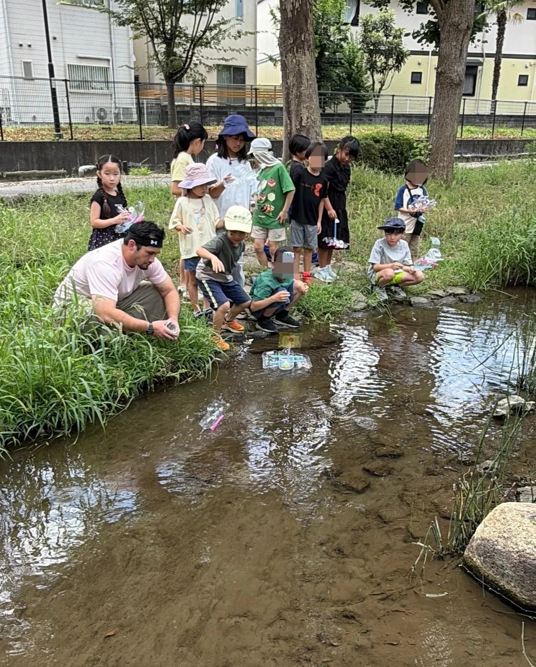 子どもたちが自分で作ったボートを先生と一緒に小川へ浮かべて試す様子